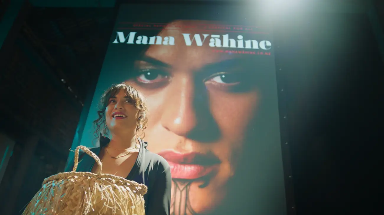 Kuīni accepts an award with her face on the cover of 'Mana Wāhine' projected behind her.