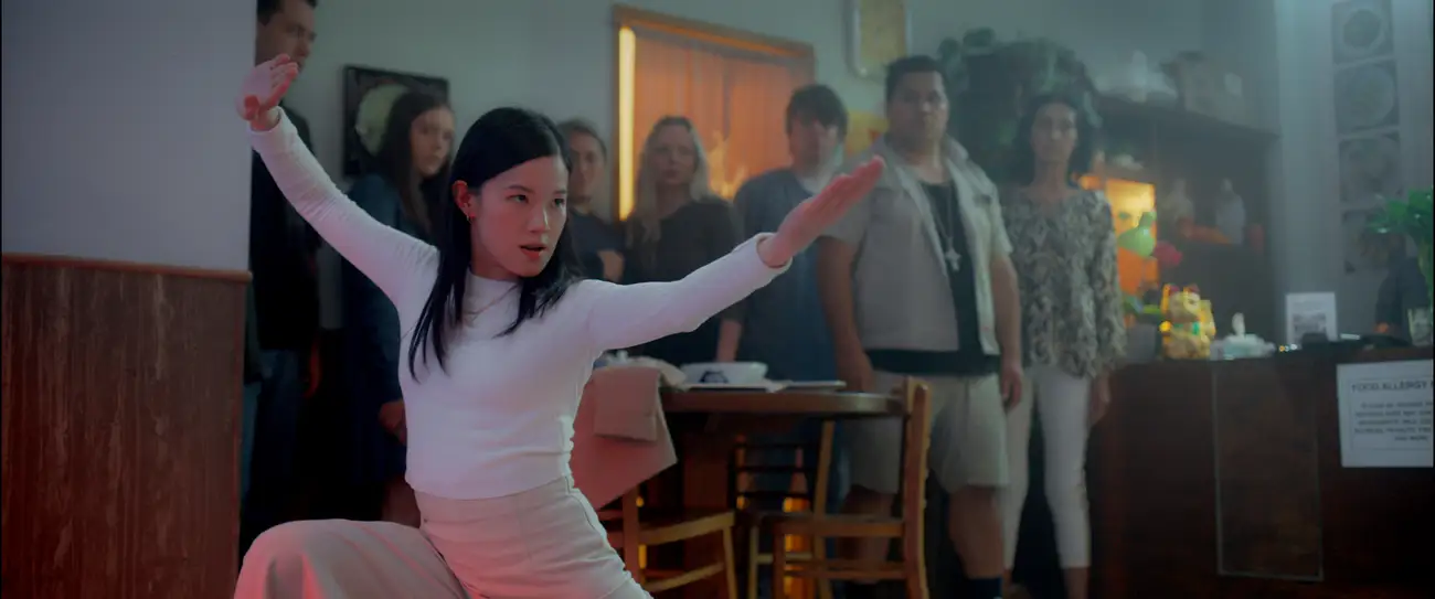 Restaurant patrons watch a Chinese woman in a kung fu stance.