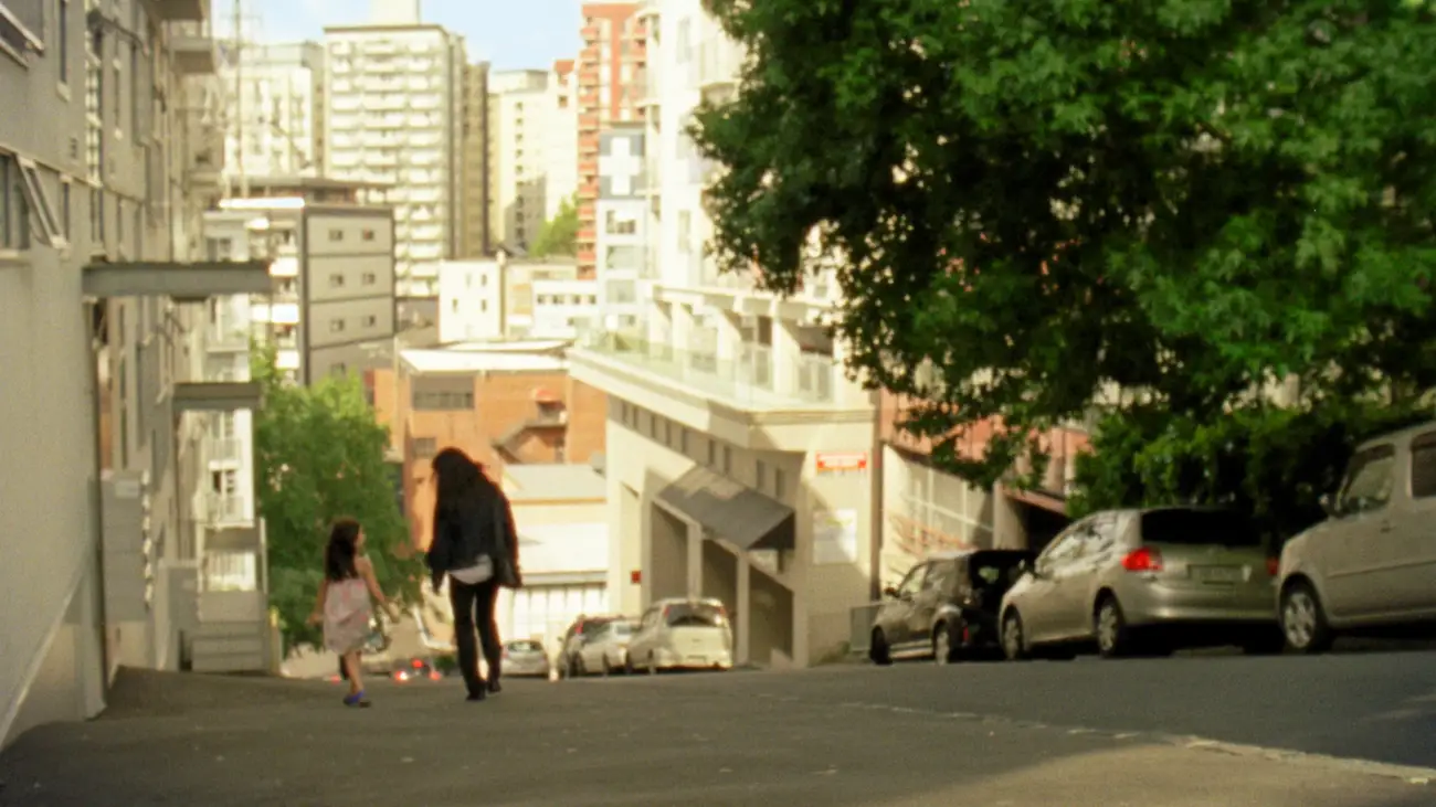 A mother and daughter walk towards a golden cityscape.
