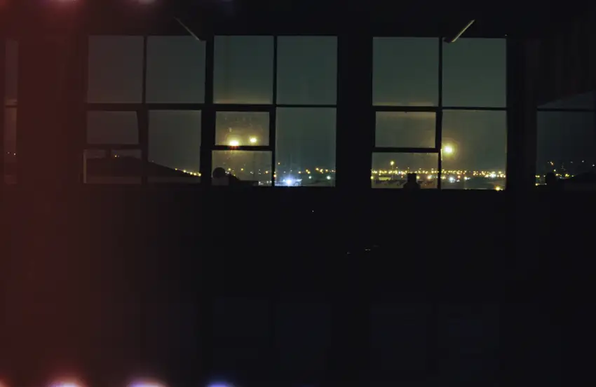 A view of Dunedin at night through dark floor-to-ceiling windows.