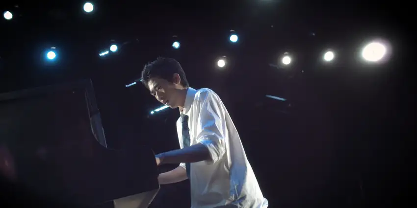 A uniformed high school student playing a piano that is collapsing into the ground.
