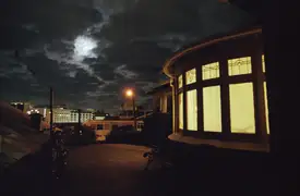 Light shining from a house in Dunedin with the moon behind clouds.