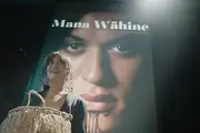 Kuīni accepts an award with her face on the cover of 'Mana Wāhine' projected behind her.