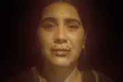 A creepy, stylistic shot of Mariana with her lips sewn.