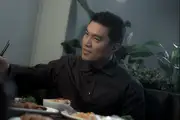 Dutch angle shot of Winson confidently deflecting chopsticks over a table full of food.