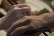 A close up of man and woman's hands touching while reaching out for food with their chopsticks.