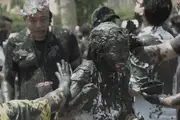 A laughing young girl getting covered in black mud by Chinese festivalgoers.