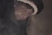 A Tibetan grandma looks down at something steaming in her kitchen.